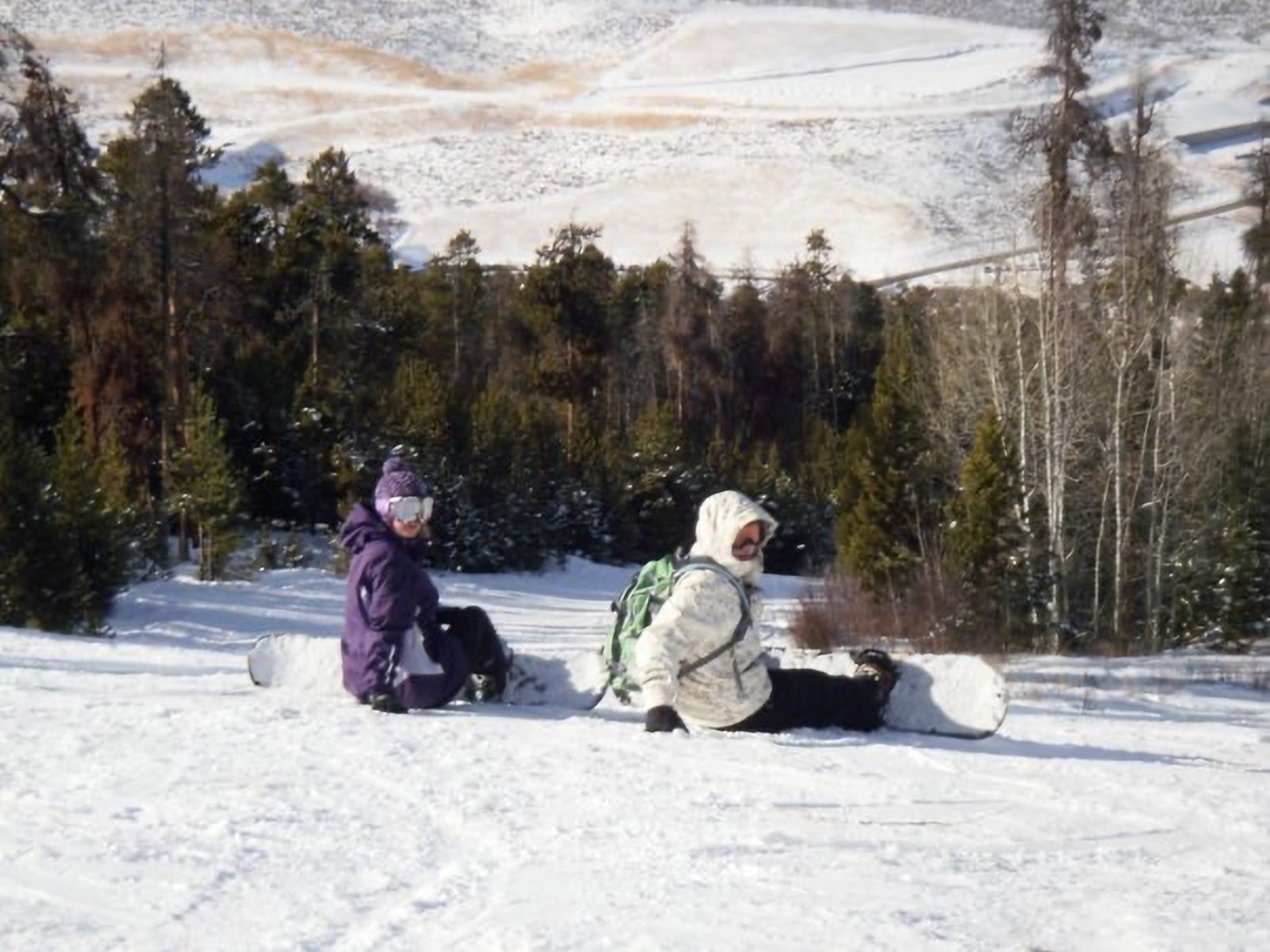 Two snowboarders taking a break on a snowy slope among pine trees